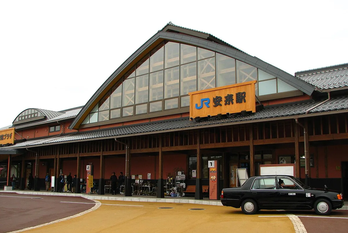 JR Yasugi Station building with a tall glazed gable, orange station sign and a taxi in front