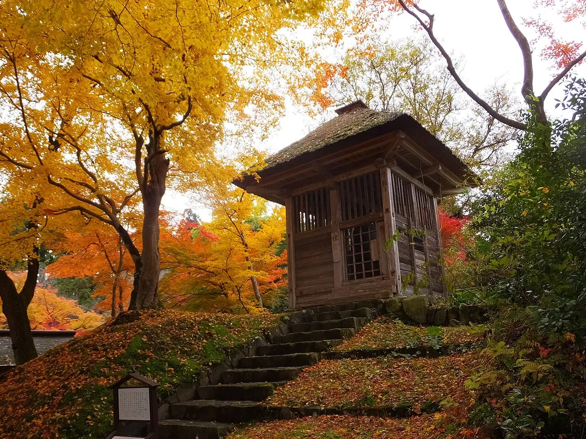 The small wooden belfry of Chusonji at the top of moss-edged stone steps, among yellow and red autumn maples
