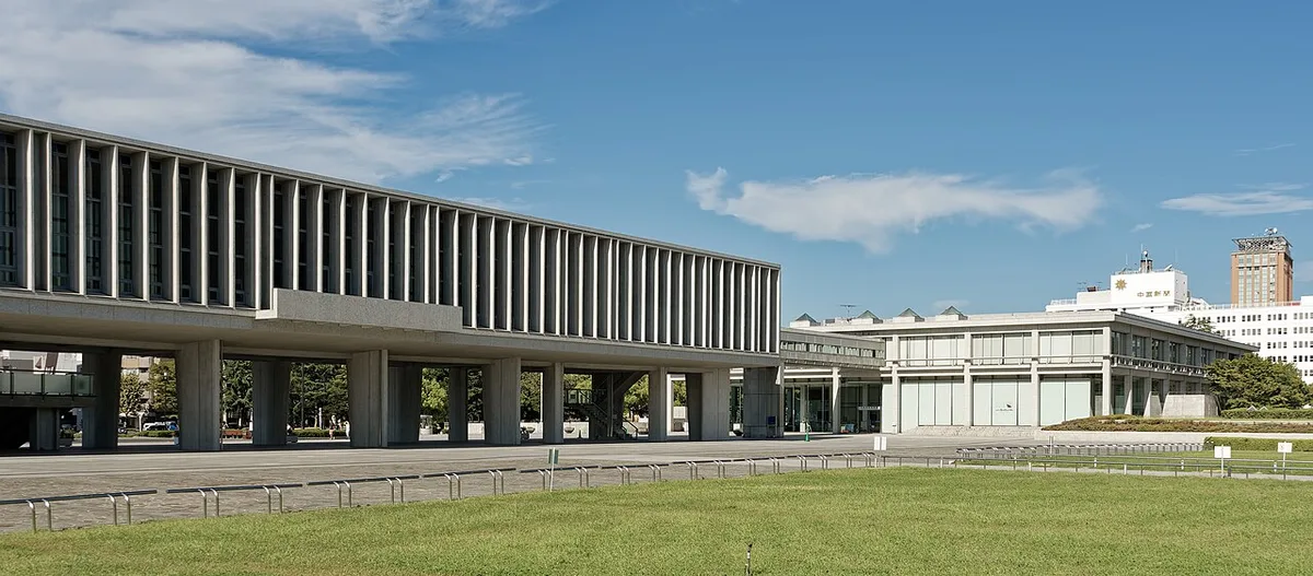 The long raised Main Building of the Hiroshima Peace Memorial Museum on pillars, with the East Building beside it, behind a lawn under a blue sky