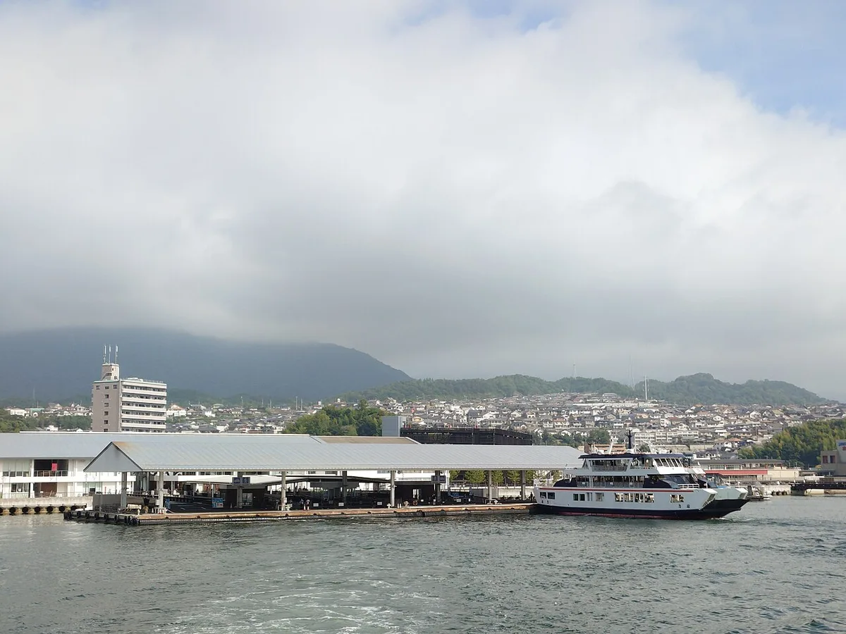 A ferry moored at the Miyajimaguchi pier, seen from the sea, with the mainland town behind