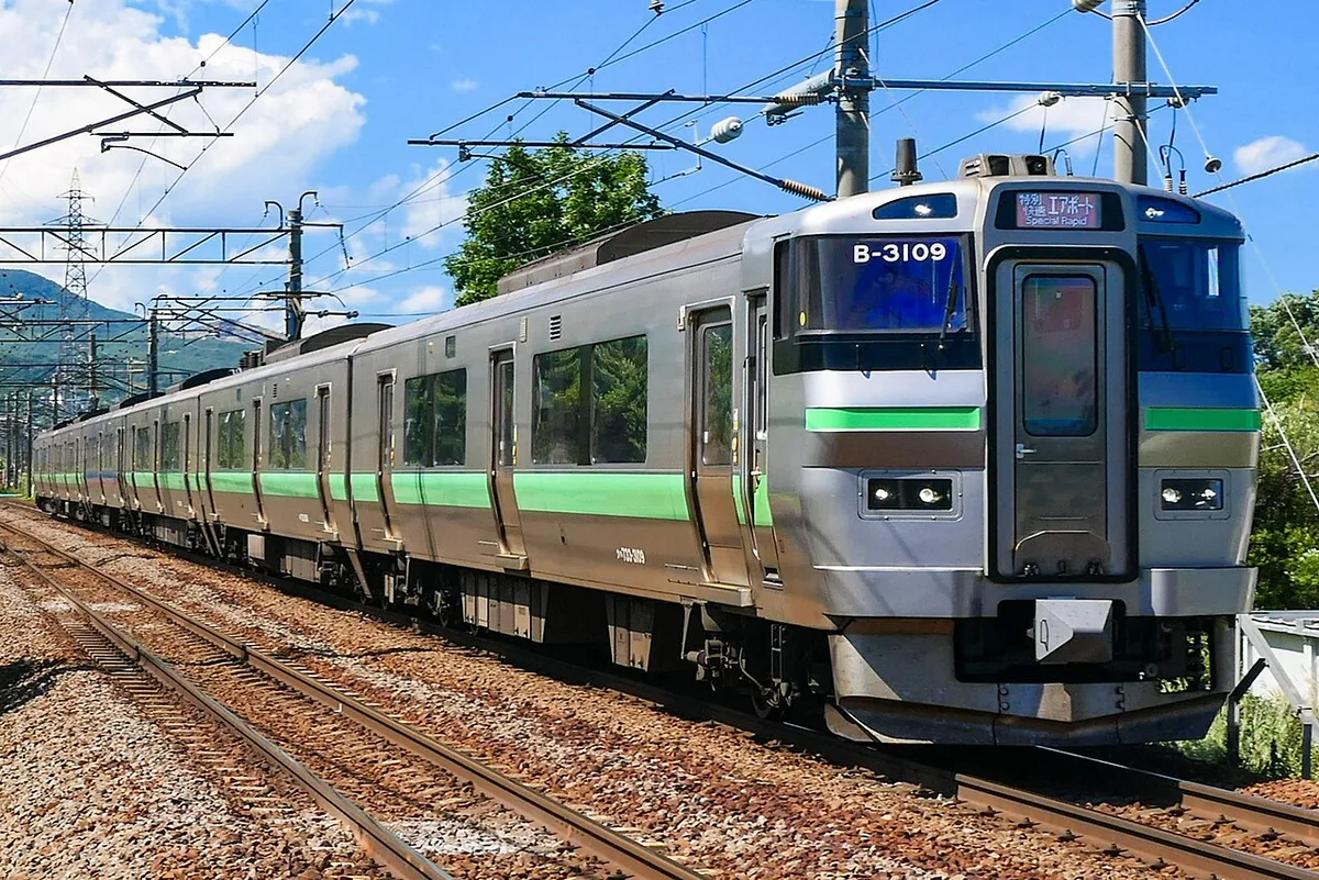 Silver JR Hokkaido 733 series electric train with green stripes on a sunny day