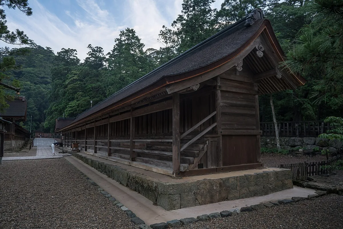 Long wooden Jukusha hall with a row of doors, among trees in the Izumo Taisha grounds