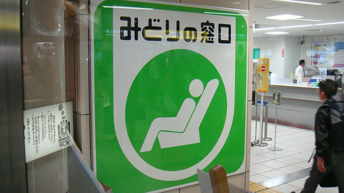 Large green Midori-no-madoguchi sign with a white reclining-seat symbol at the entrance of a JR ticket office, with the service counter behind it