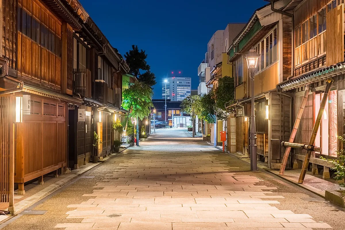 Empty stone-paved street of wooden teahouses in the Nishi Chaya district of Kanazawa at dusk, lit by street lamps