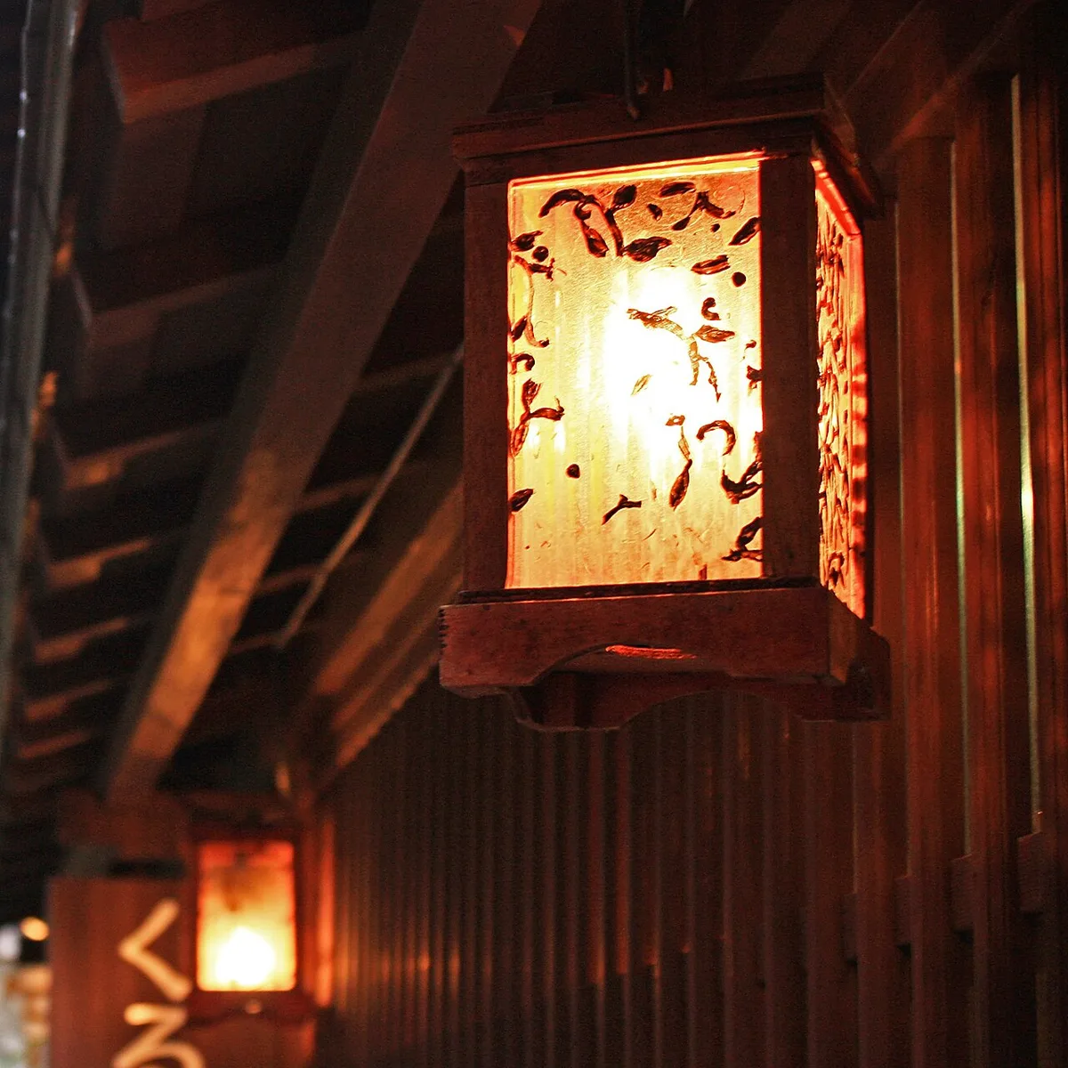 Lit paper lantern hanging under the eaves of a wooden teahouse in Higashi Chaya at night