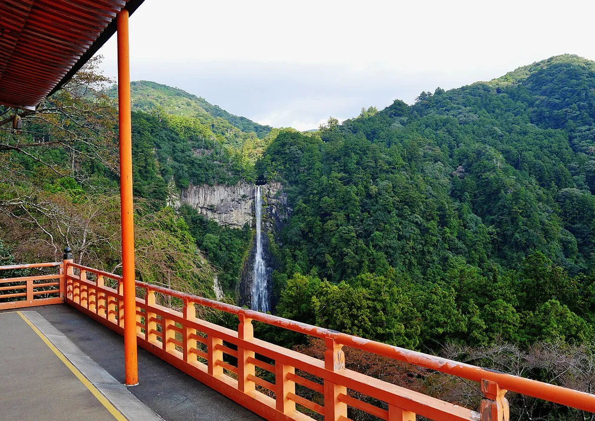 Nachi Falls dropping down a forested mountainside, framed by the vermilion railing of a pagoda balcony