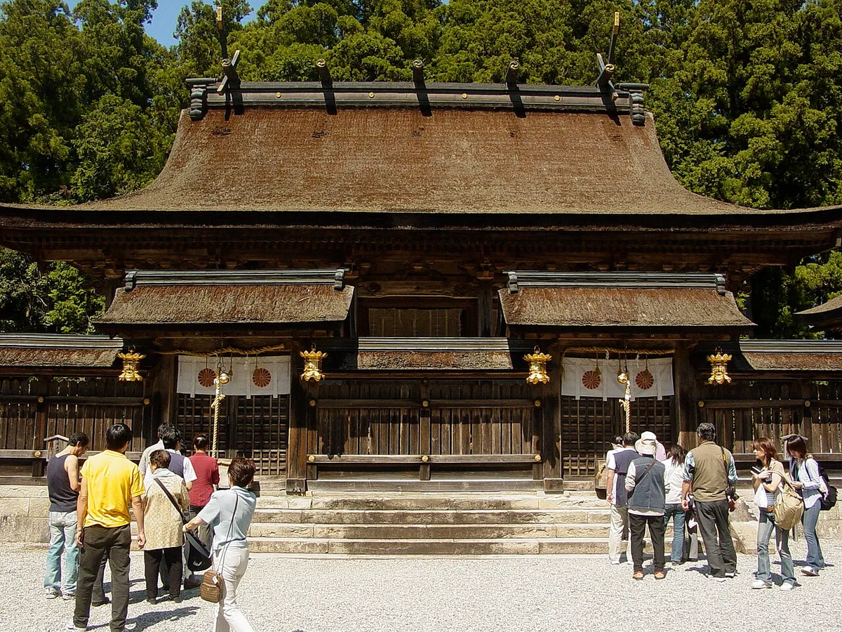Visitors in front of the cypress-bark-roofed main halls of Kumano Hongu Taisha, hung with white curtains and gold lanterns
