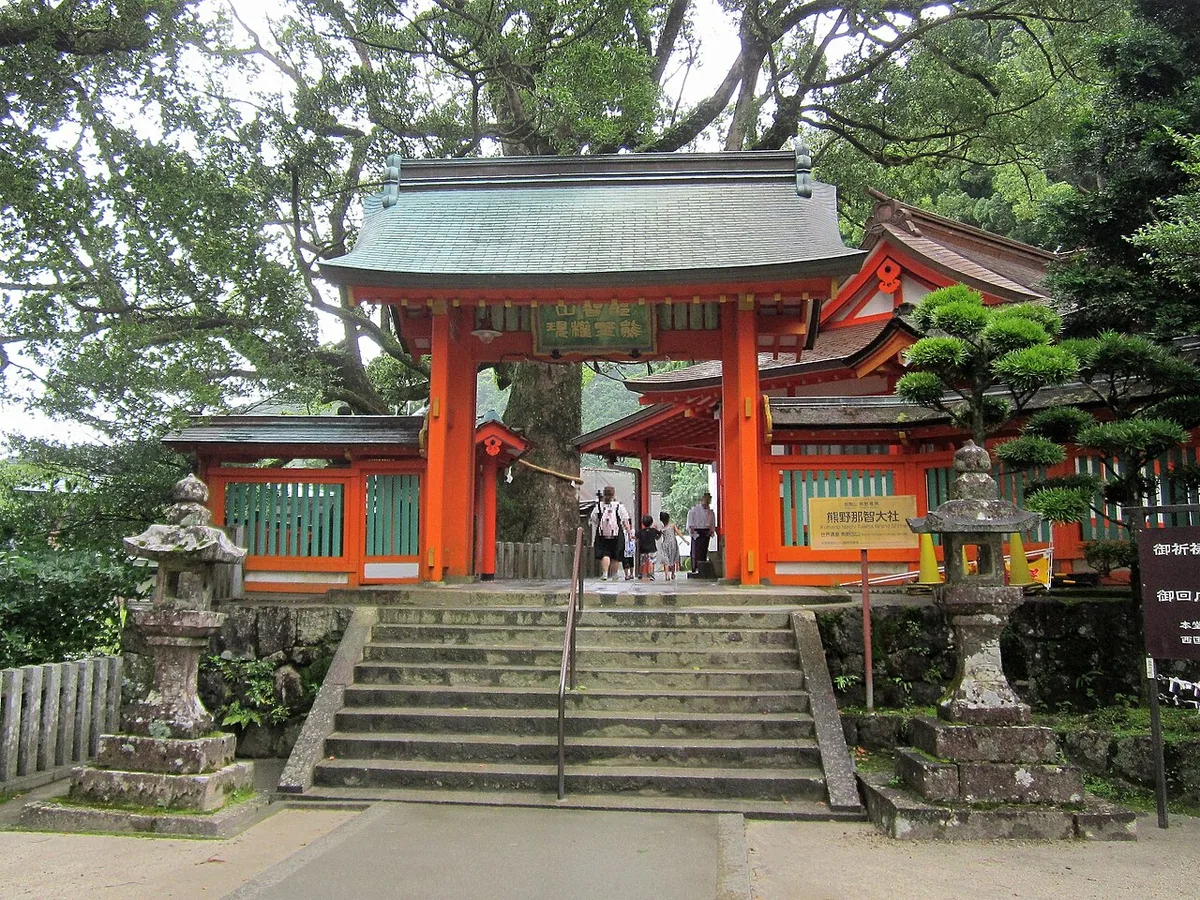 Stone steps and lanterns leading up to the vermilion gate of Kumano Nachi Taisha under a large camphor tree