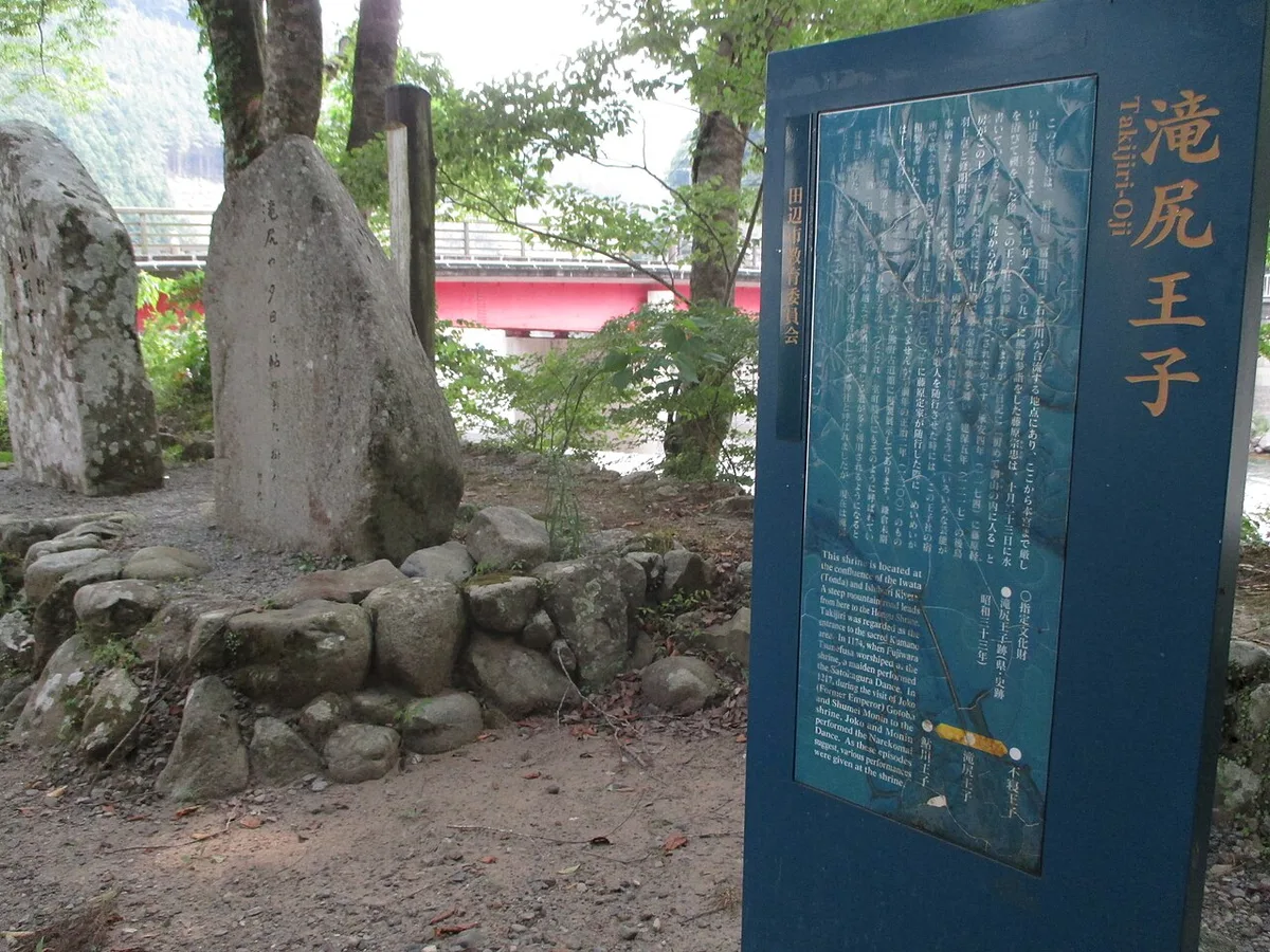The Takijiri-oji information board and old stone monuments at the trailhead, with a red bridge behind