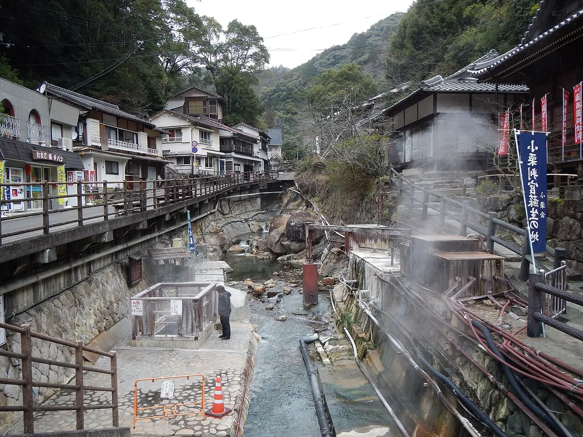 Steam rising from hot springs along the stream through Yunomine Onsen, with inns and a footbridge on both banks