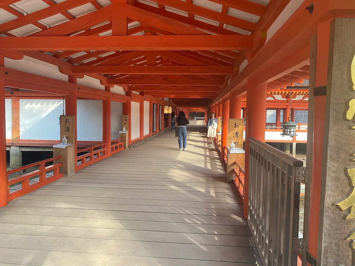 A long vermilion roofed corridor with a plank floor inside Itsukushima Shrine on Miyajima