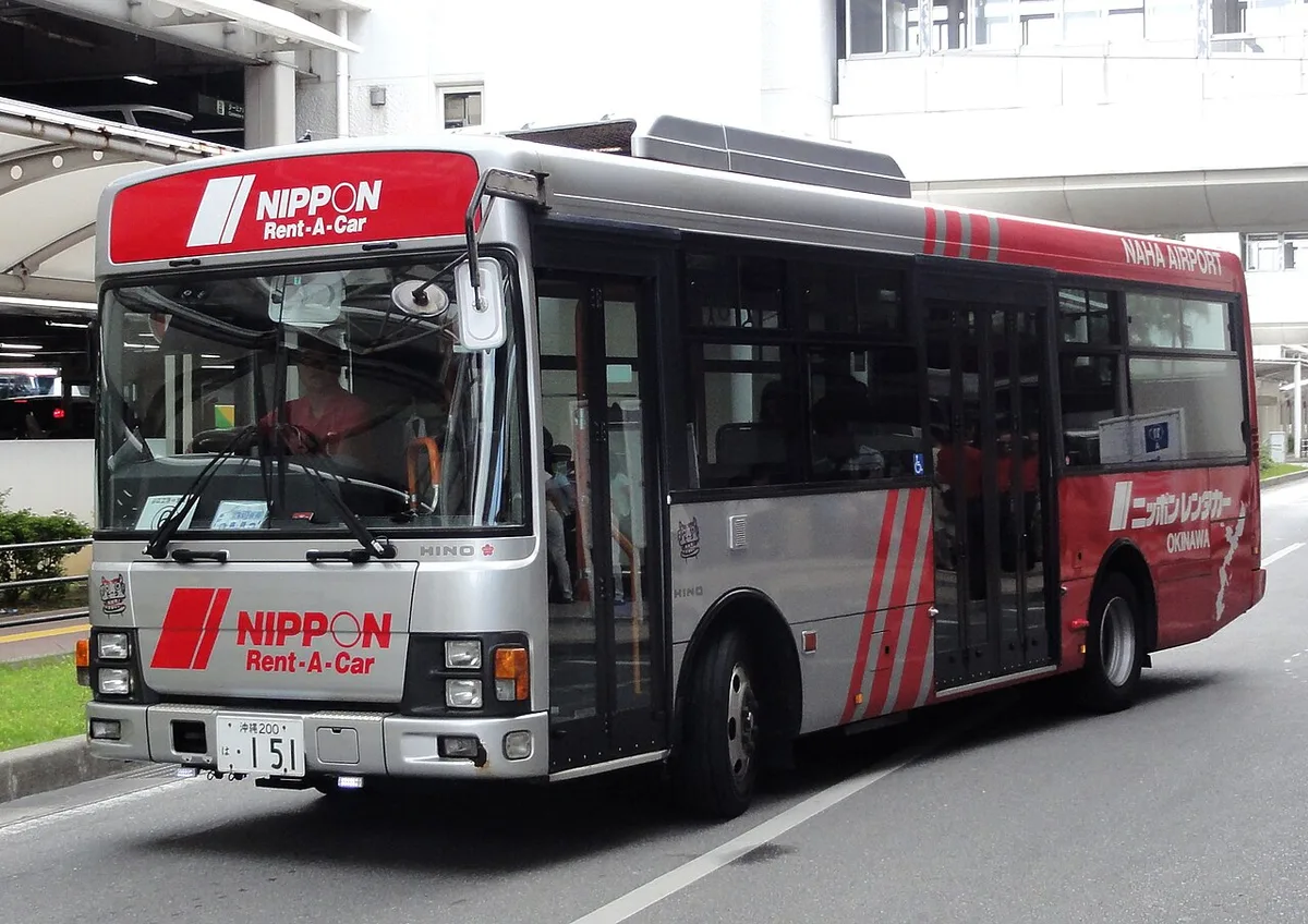 Red and silver Nippon Rent-A-Car shuttle bus marked Naha Airport, parked at the kerb outside the airport terminal