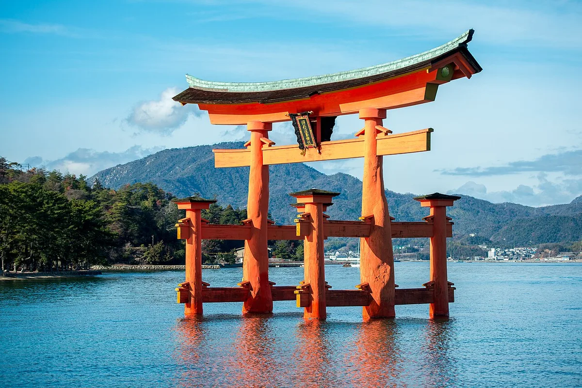 The vermilion Otorii gate standing in the sea off Itsukushima Shrine, with the hills of Miyajima behind