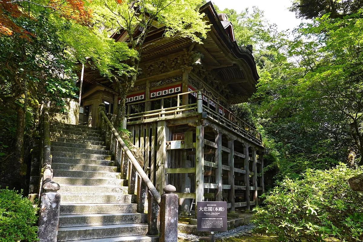 Stone steps up to Daihikaku, the main hall of Natadera, built against the rock among green maples, Komatsu