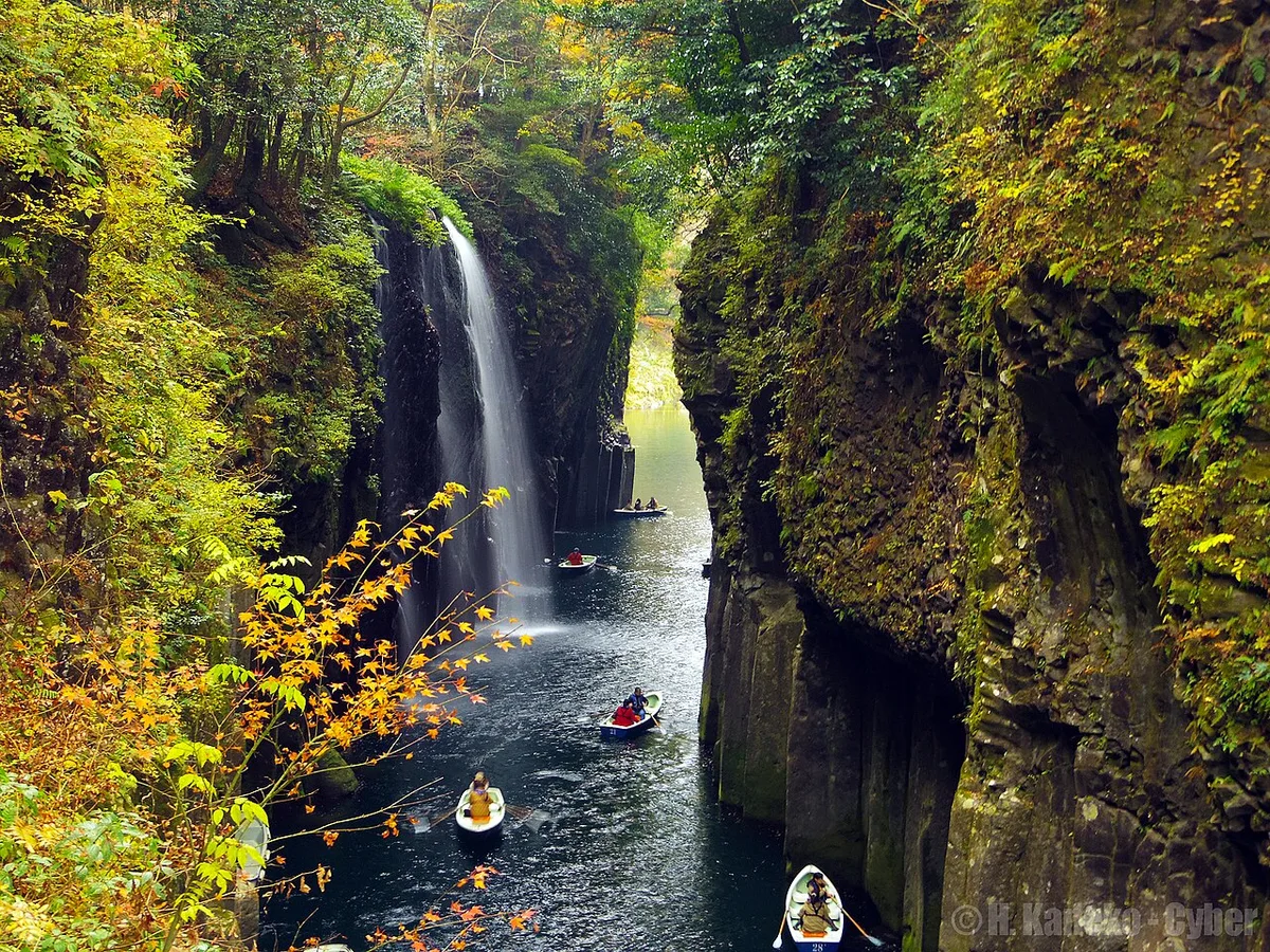 Rowing boats on the river in Takachiho Gorge below Manai Falls and basalt cliffs, with autumn leaves