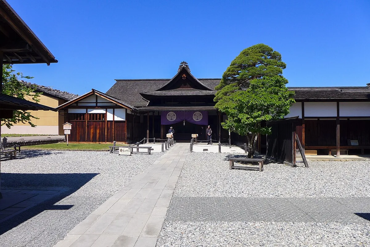 Gravel courtyard and stone path leading to the main entrance of Takayama Jinya, with purple curtains and a pine tree