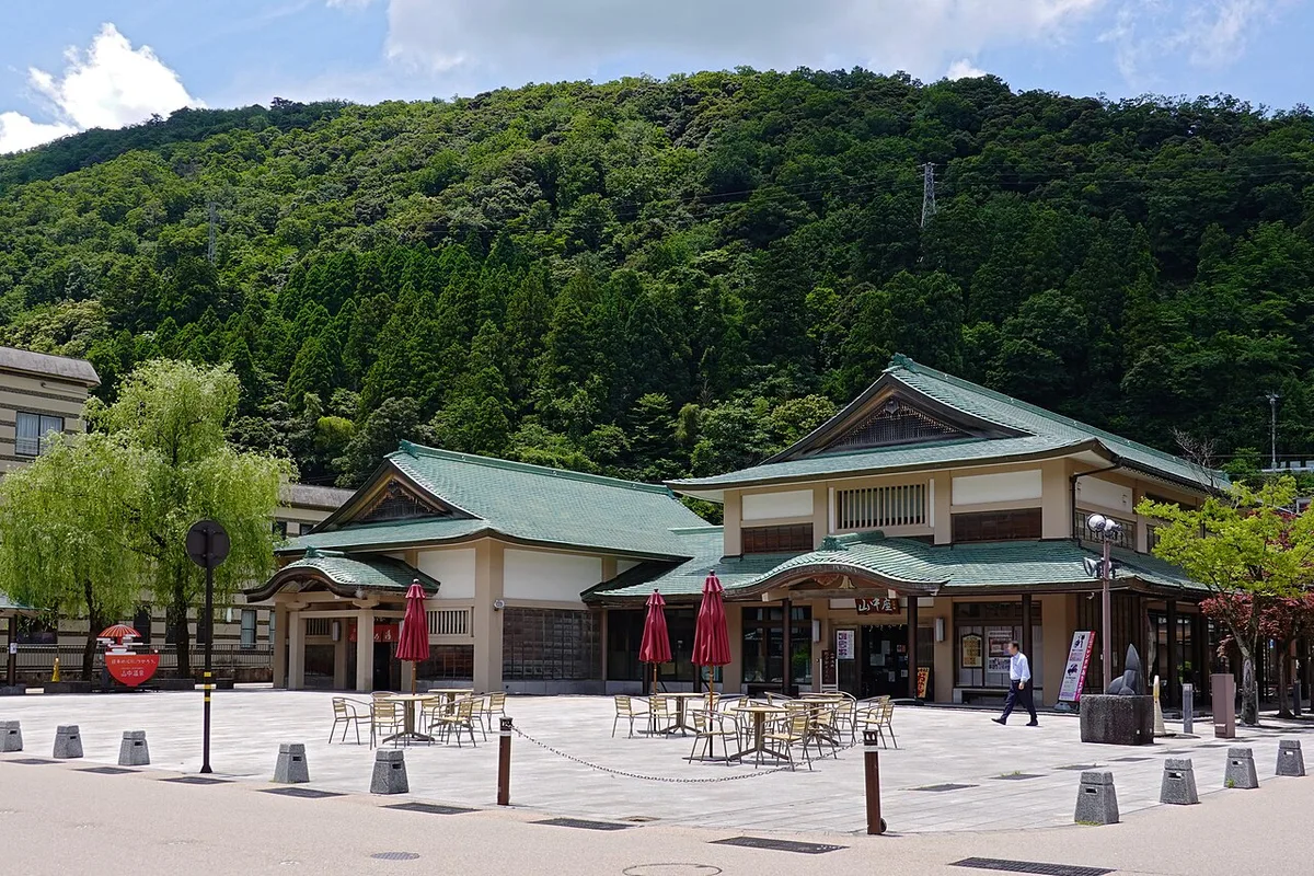 Kiku no Yu public bath, a two-winged building with green tiled roofs on a paved square below a wooded hill