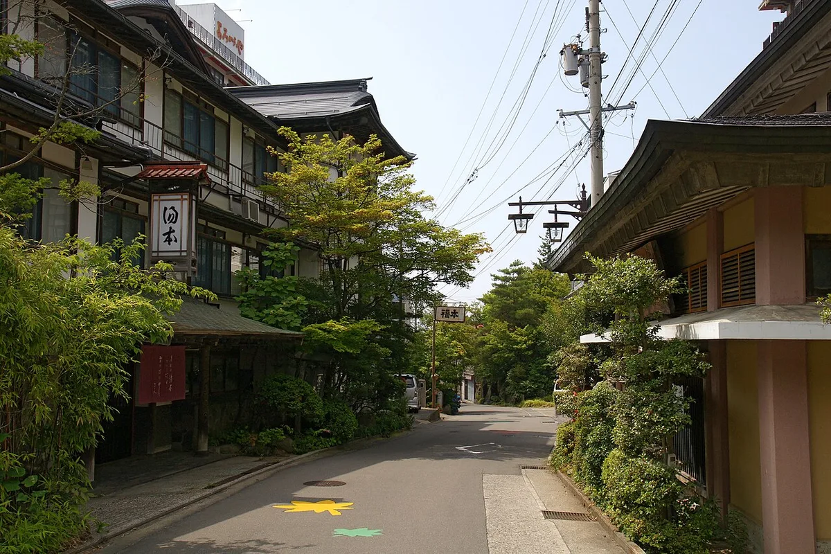 Multi-storey wooden ryokan with a hanging sign beside a quiet street in Yudanaka Onsen