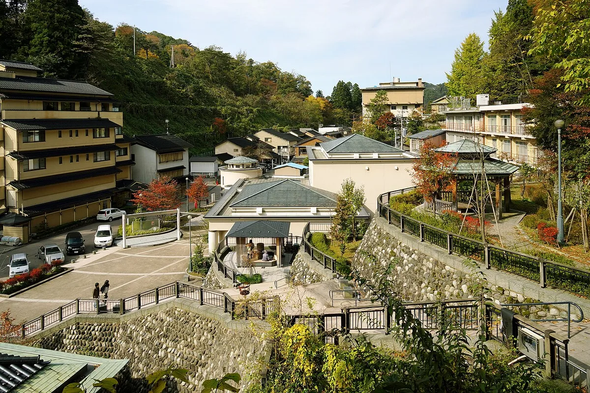 Yuwaku Onsen seen from above, with inns, a hillside garden path and a pavilion among autumn trees