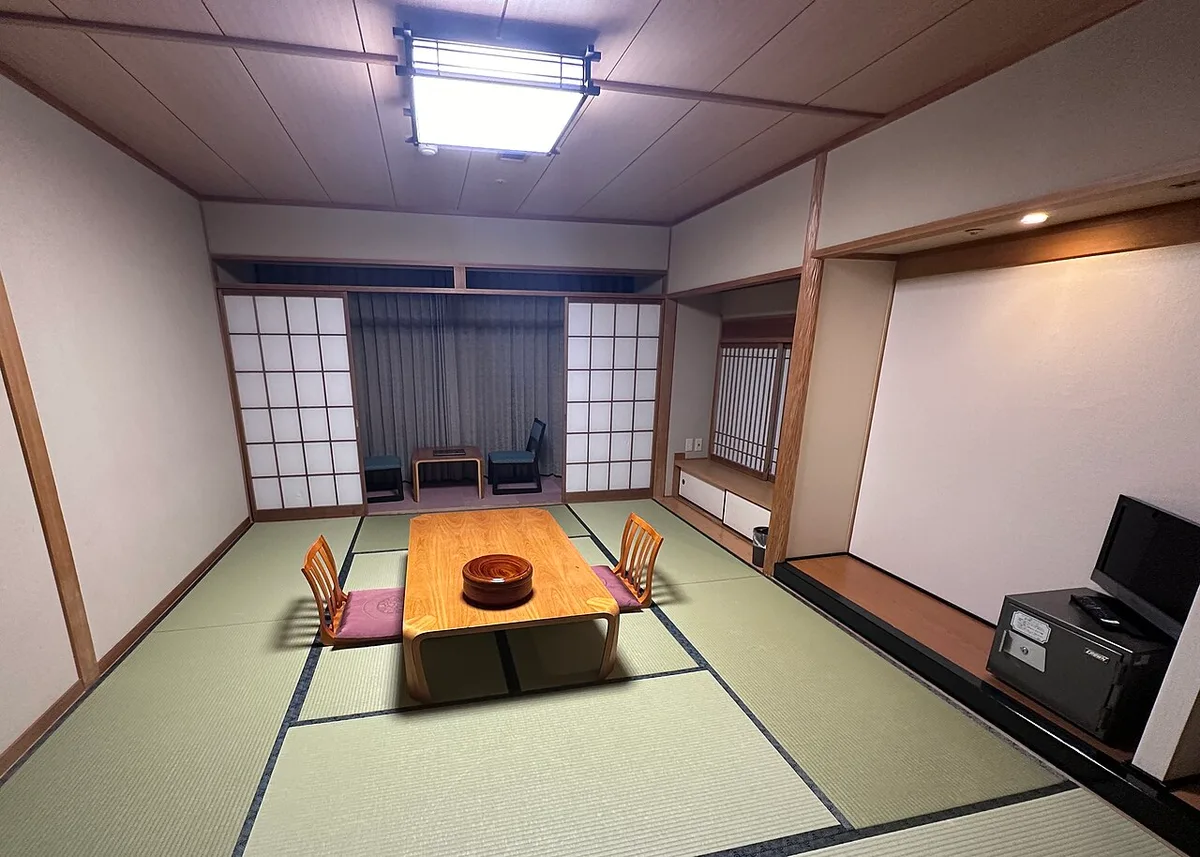 Empty ryokan guest room with green tatami mats, a low wooden table with legless chairs and shoji screens at the window