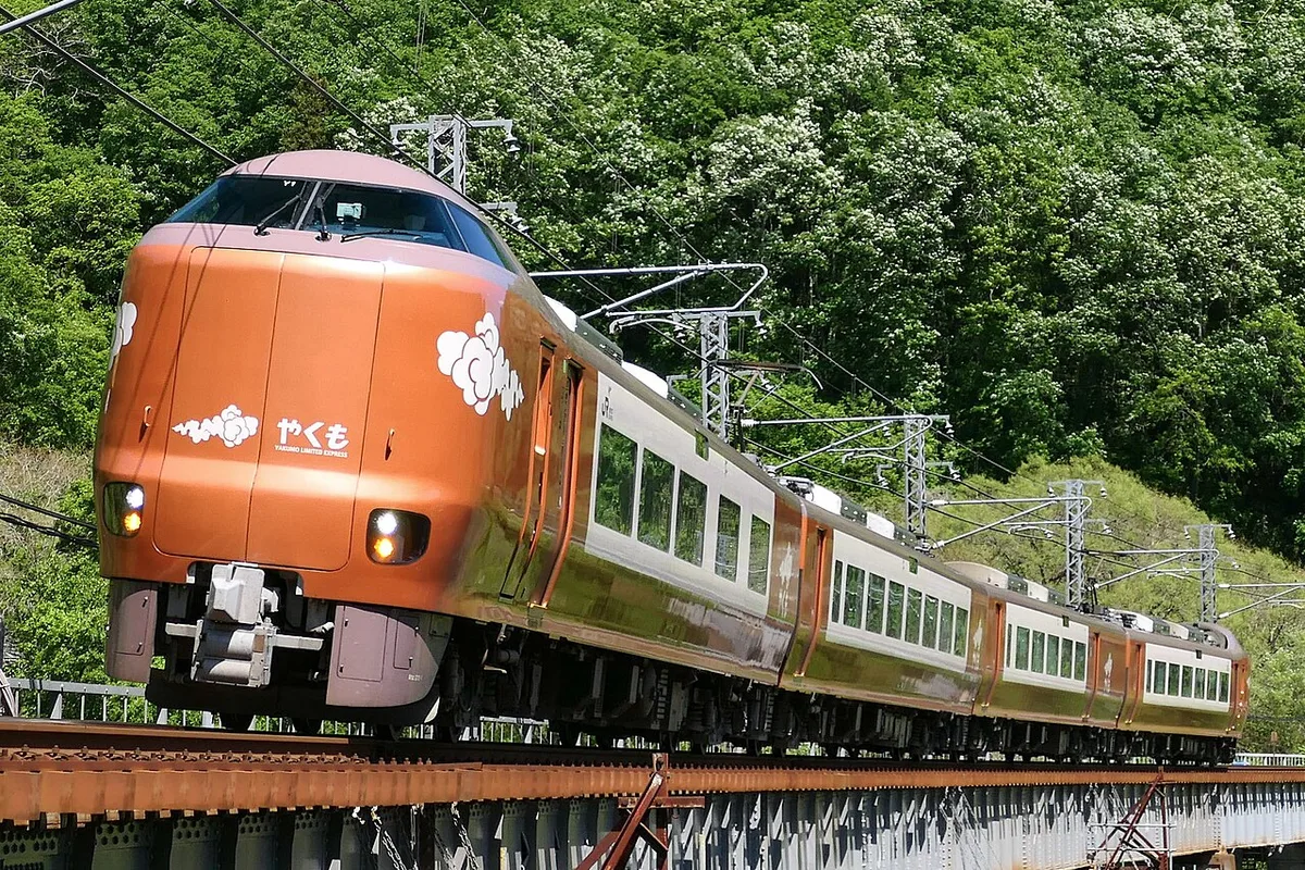 Copper-coloured 273 series Yakumo limited express crossing a bridge past green hillsides