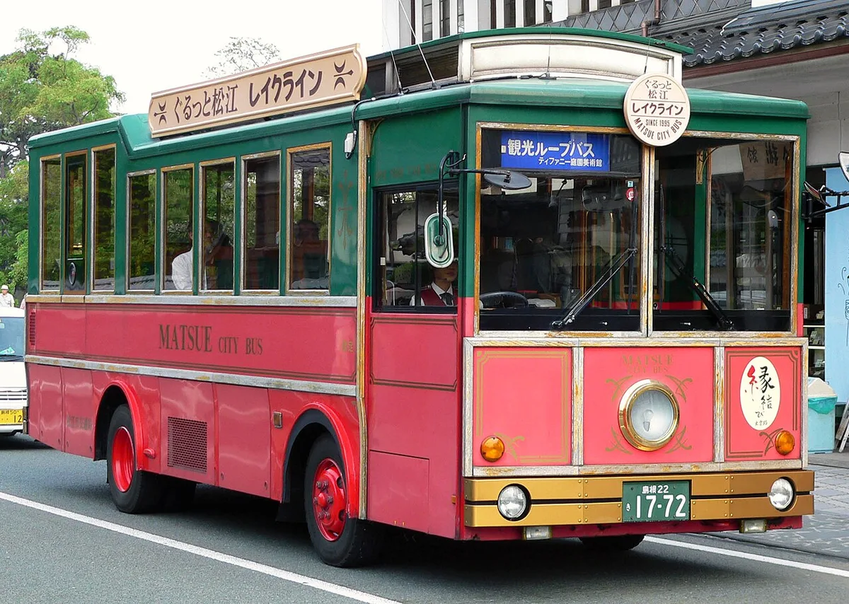 Red and green retro-style Lake Line loop bus on a street in Matsue