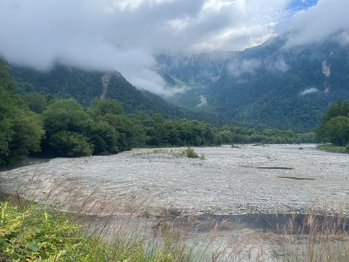 The wide gravel bed of the Azusa River at Kamikochi with forested mountains under low cloud