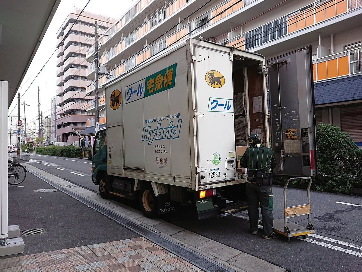 Yamato Transport delivery truck with its rear doors open and a driver loading parcels from a hand cart