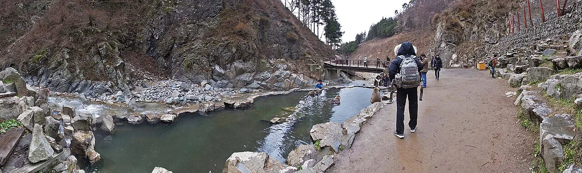 Panorama of the rocky river valley at Jigokudani Yaen-koen, a pool by the path and visitors walking along it