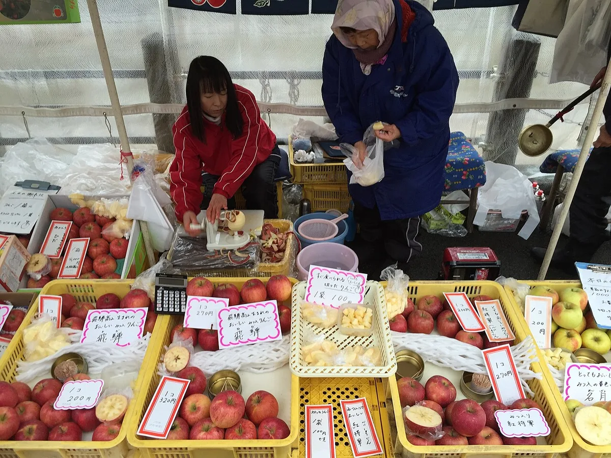 Stallholders selling Hida apples in yellow crates under a tent at the Miyagawa morning market in Takayama