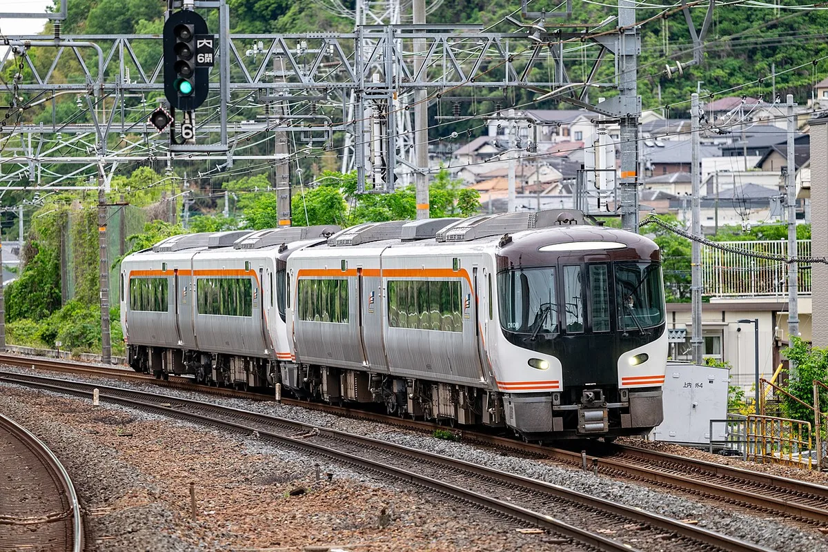 A silver HC85 series Hida limited express train with orange stripes running on double track under overhead wires