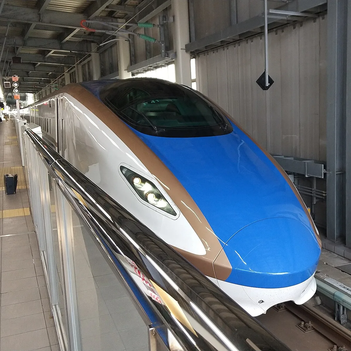 Blue, copper and white nose of a W7 series Hokuriku Shinkansen train at a platform