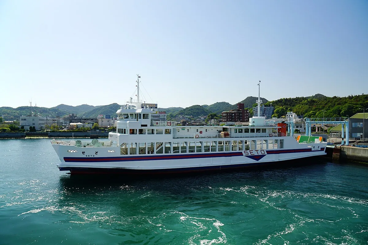 White car ferry turning in the green water of Uno Port, with the town and hills behind