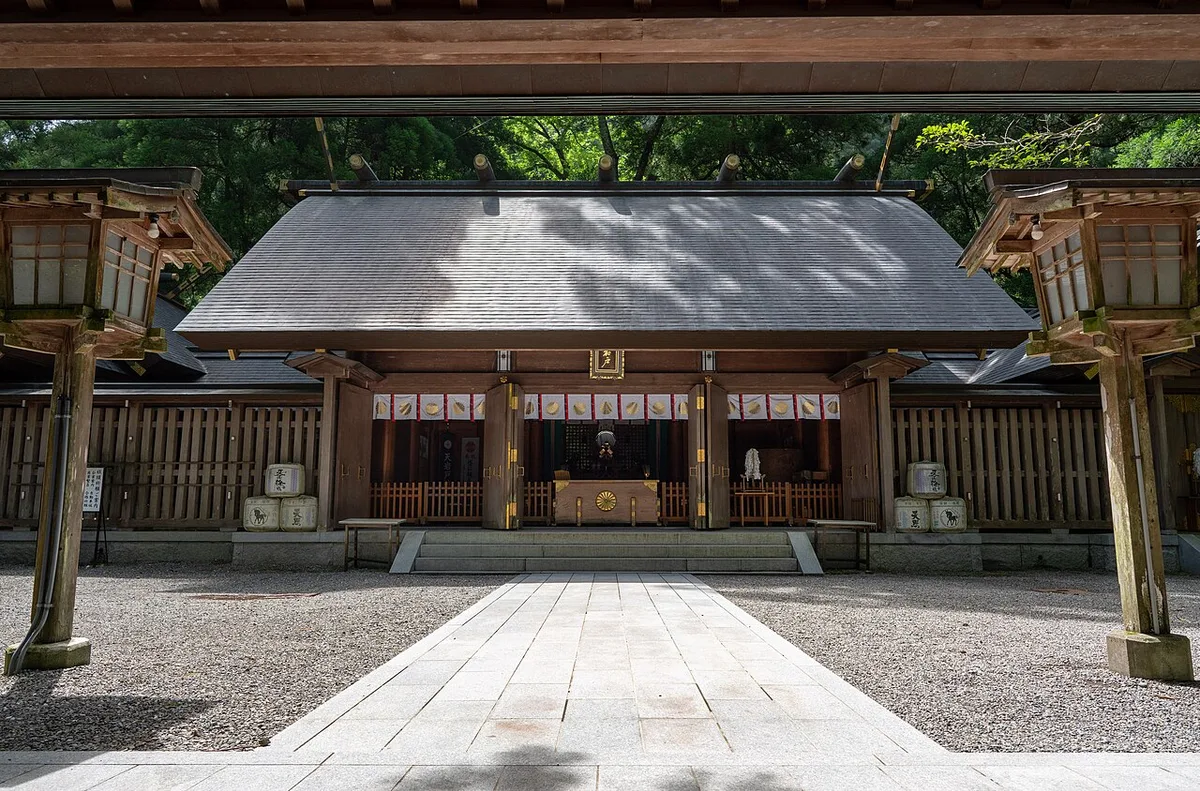 Wooden main hall of the West Shrine of Amano Iwato Shrine framed by a gate roof and stone lanterns