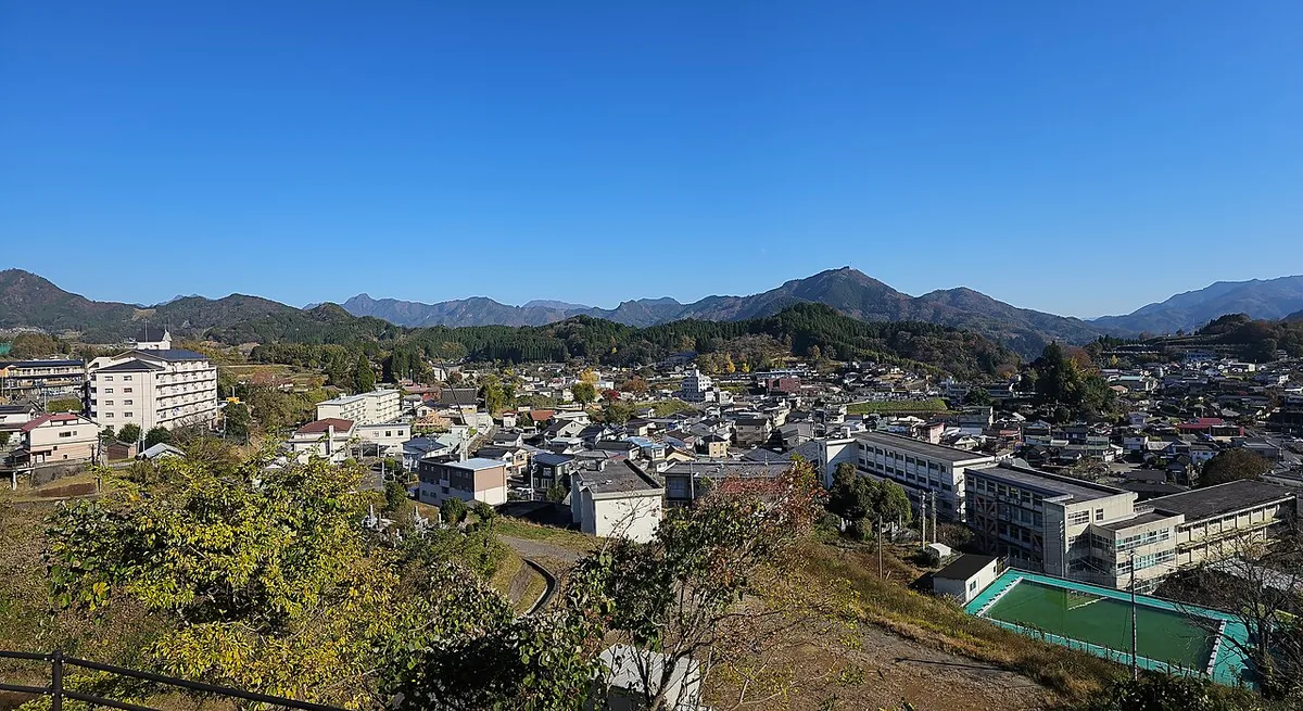 View over the rooftops and hotels of central Takachiho town with forested mountains behind under a clear blue sky