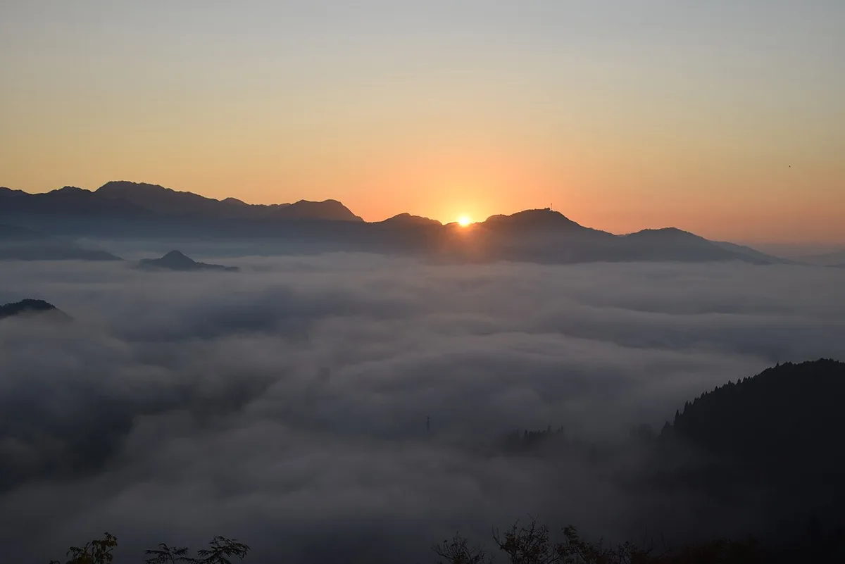 A sea of clouds filling the valleys below Kunimigaoka at sunrise, with mountain ridges behind
