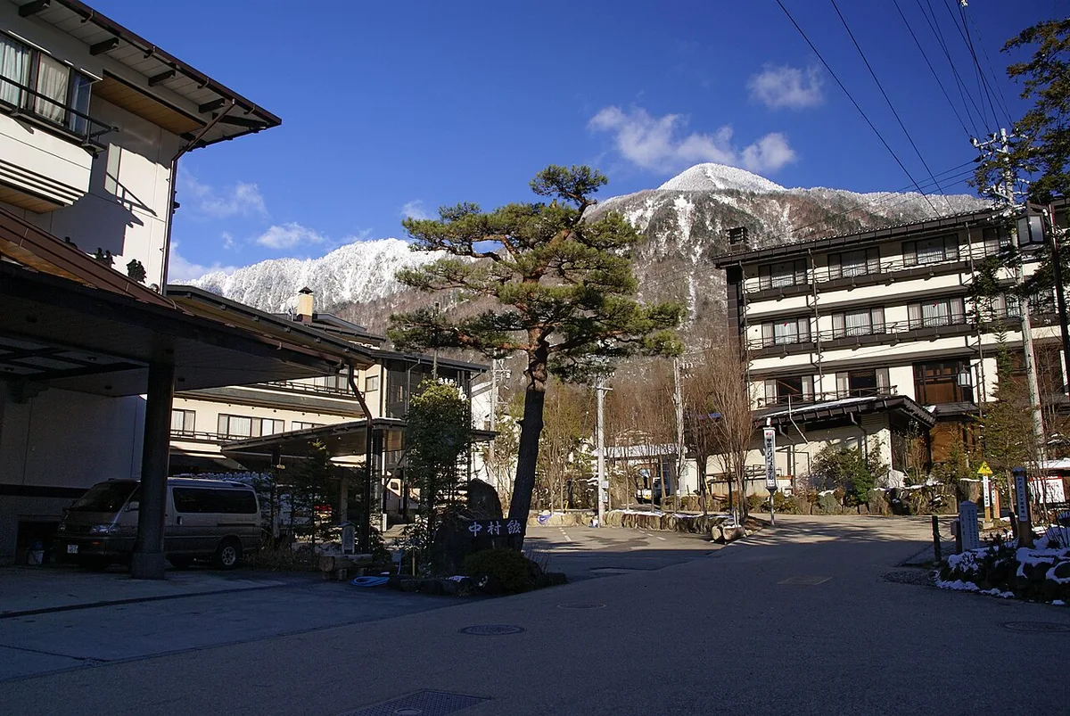 Inns along a street in Hirayu Onsen with snow-covered mountains behind, Okuhida