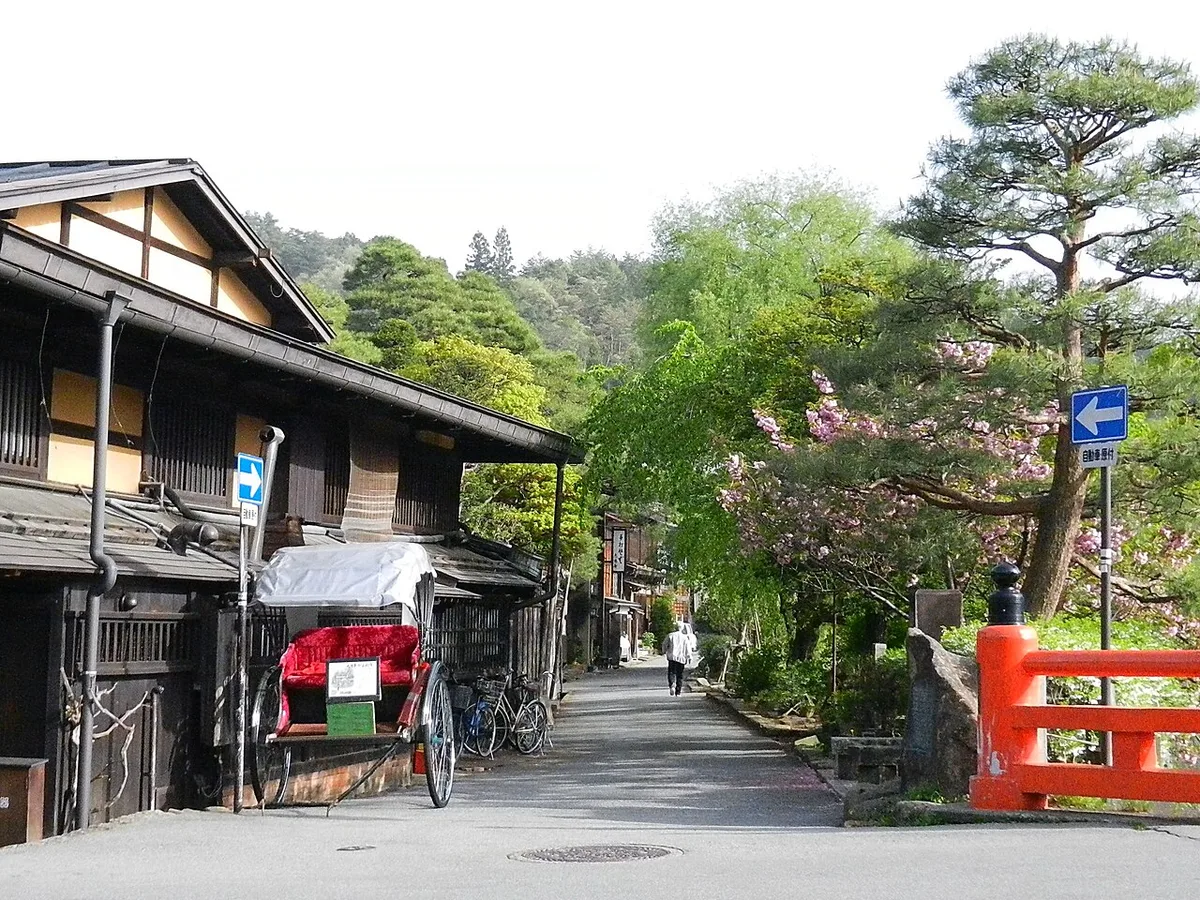 Old wooden houses and a rickshaw on a street beside the red Nakabashi bridge, Takayama